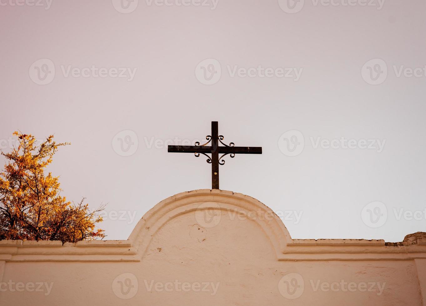 cruz na capela fotografada de baixo contra um fundo de céu claro e madeira foto