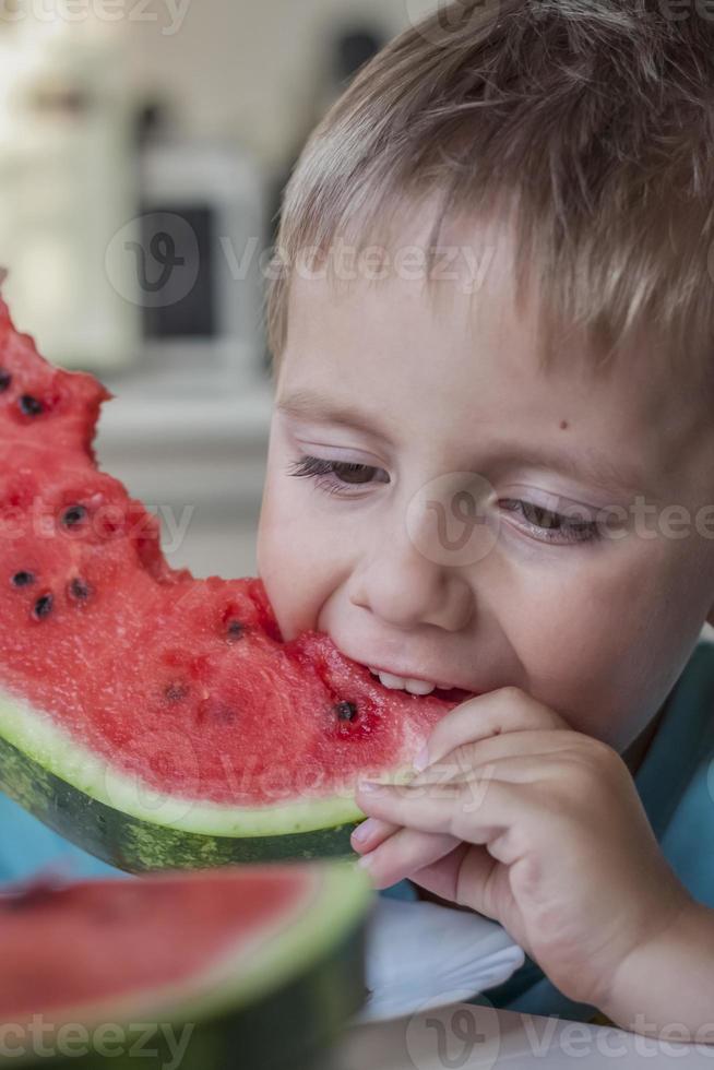 menino bonito comendo melancia em casa. emoções reais sem posar. foto