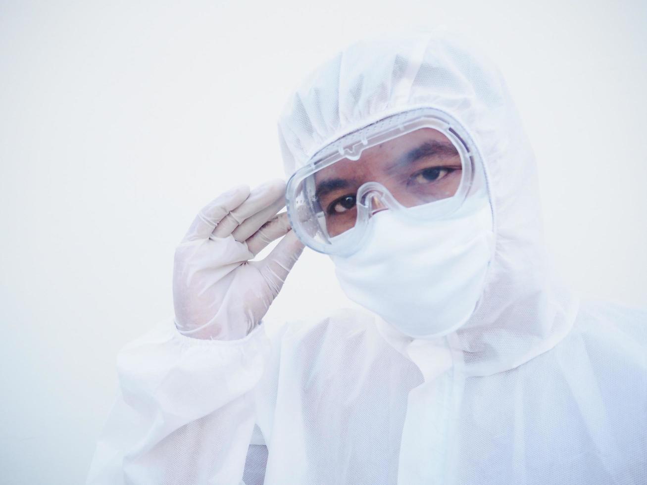 closeup de jovem médico asiático ou cientista em uniforme de suíte de ppe segurando óculos com as mãos enquanto olha para a frente. coronavírus ou covid-19 conceito isolado fundo branco foto