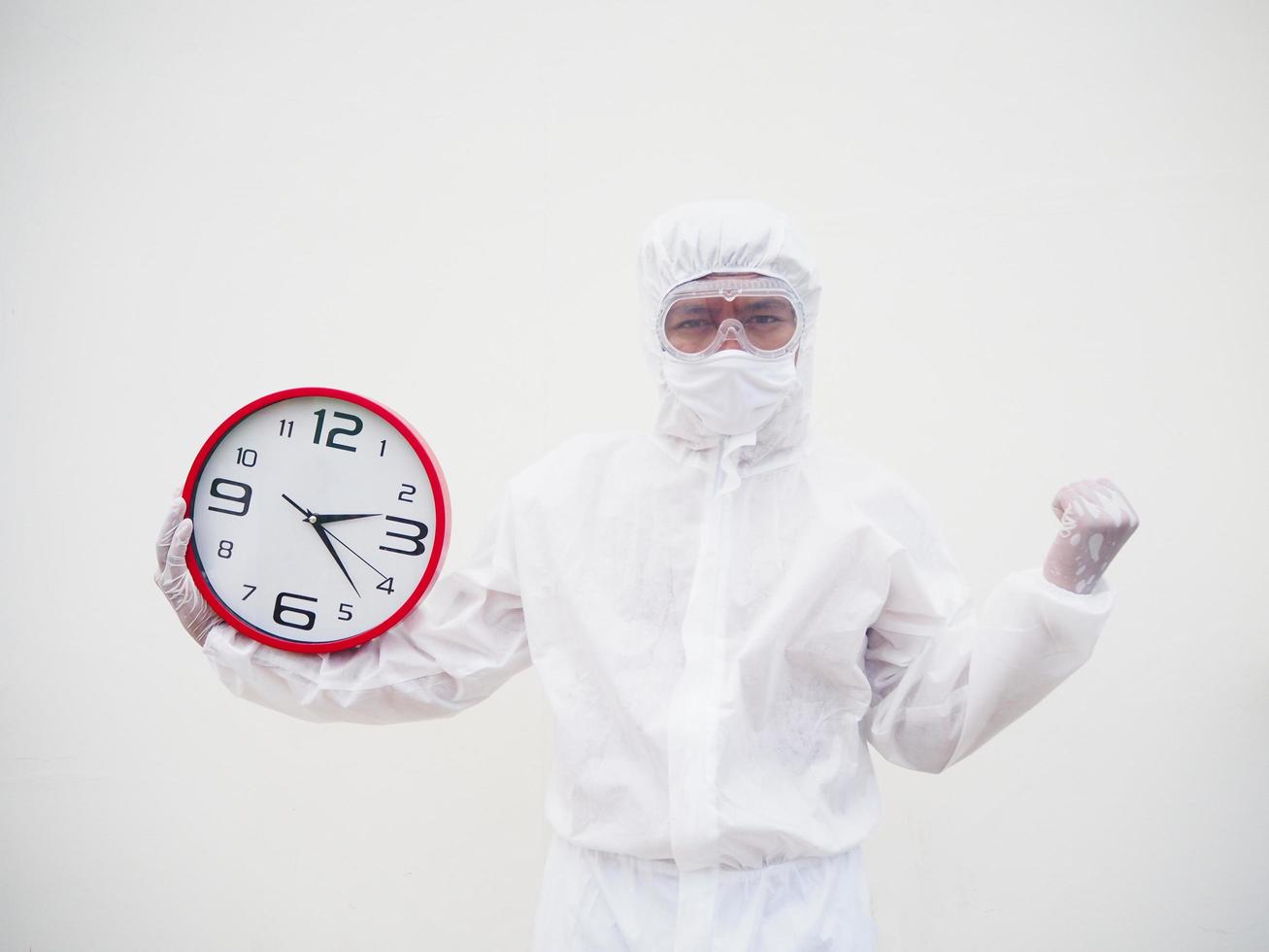 retrato de médico ou cientista em uniforme de suíte de ppe segurando o despertador vermelho e olhando para a câmera em vários gestos. fundo branco isolado conceito covid-19 foto