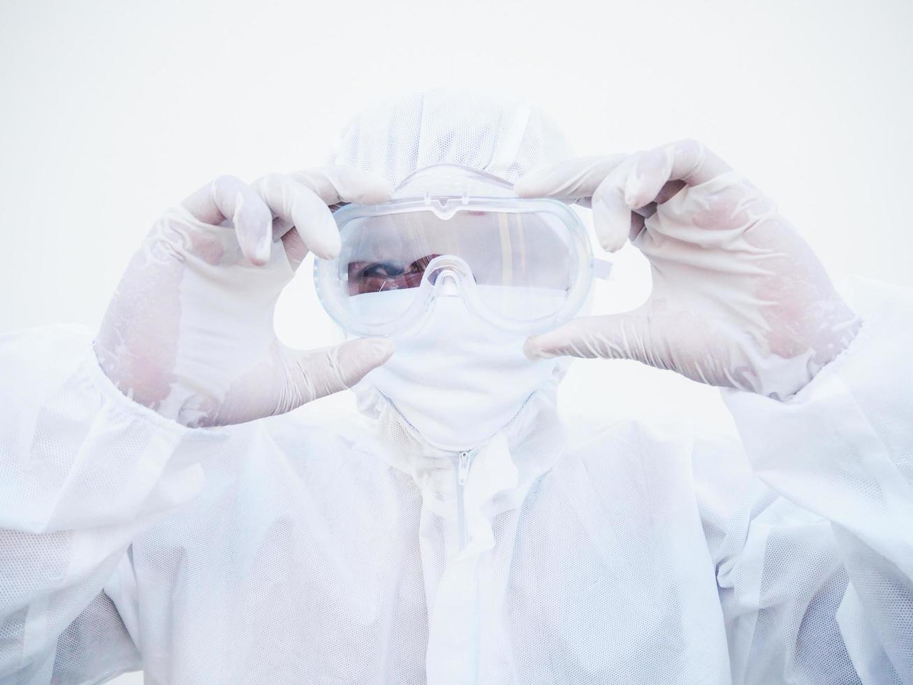 closeup de jovem médico asiático ou cientista em uniforme de conjunto de ppe segurando os óculos com as duas mãos enquanto olha para a frente. coronavírus ou covid-19 conceito isolado fundo branco foto