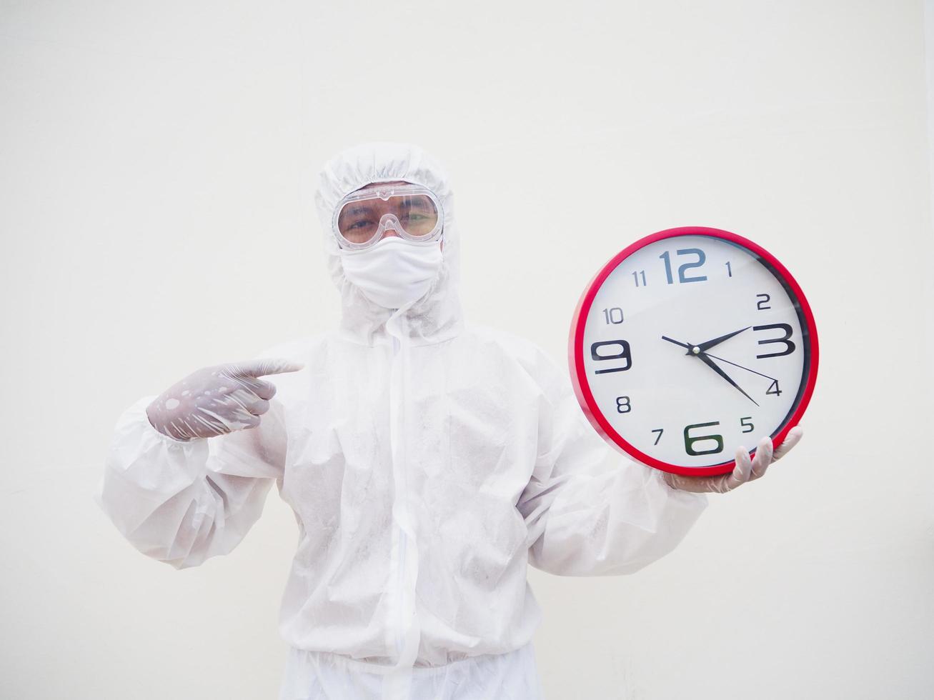 retrato de médico ou cientista em uniforme de suíte de ppe segurando o despertador vermelho e olhando para a câmera em vários gestos. fundo branco isolado conceito covid-19 foto