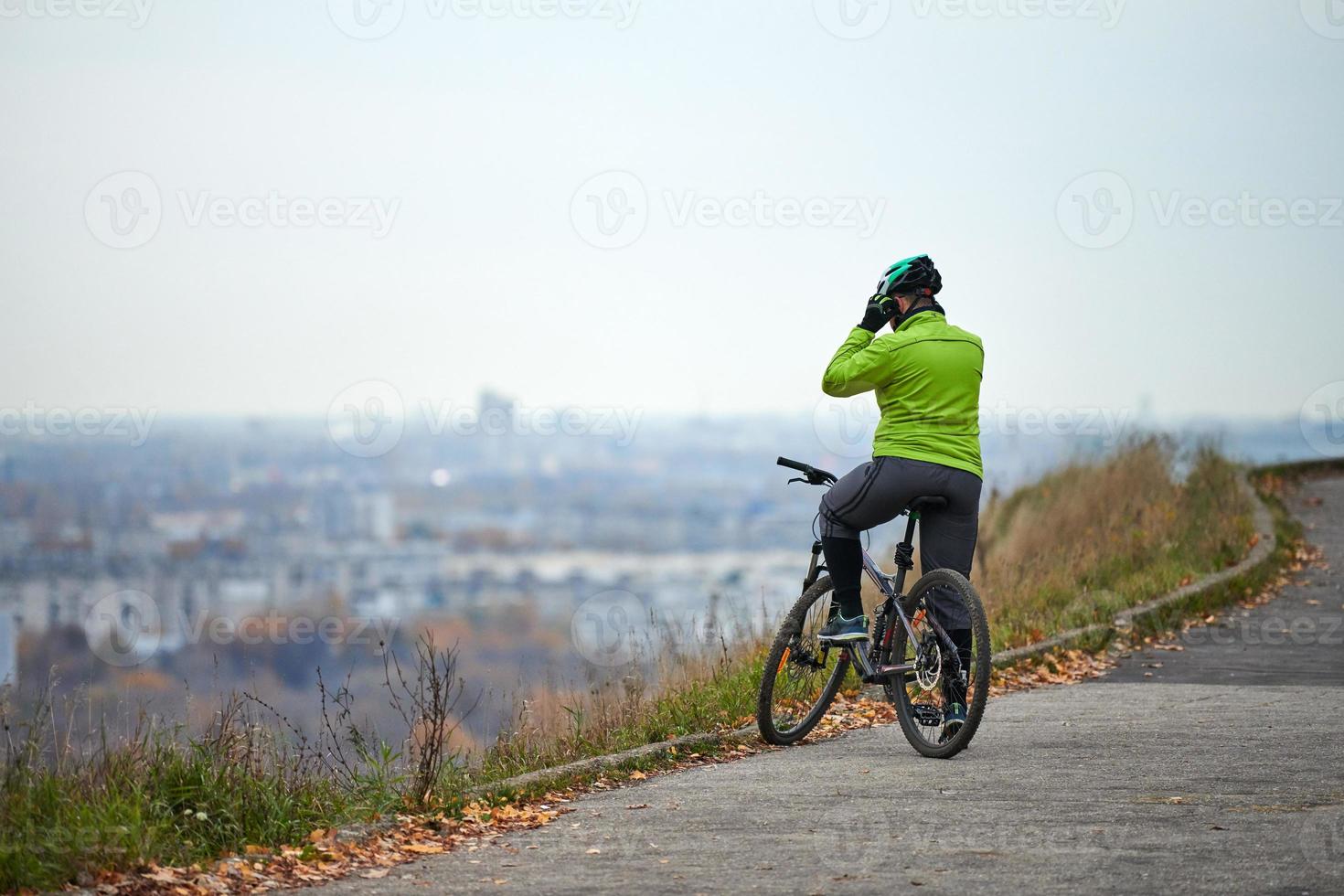 ciclista no topo da colina olhando para a paisagem urbana, vista traseira, copie o espaço foto
