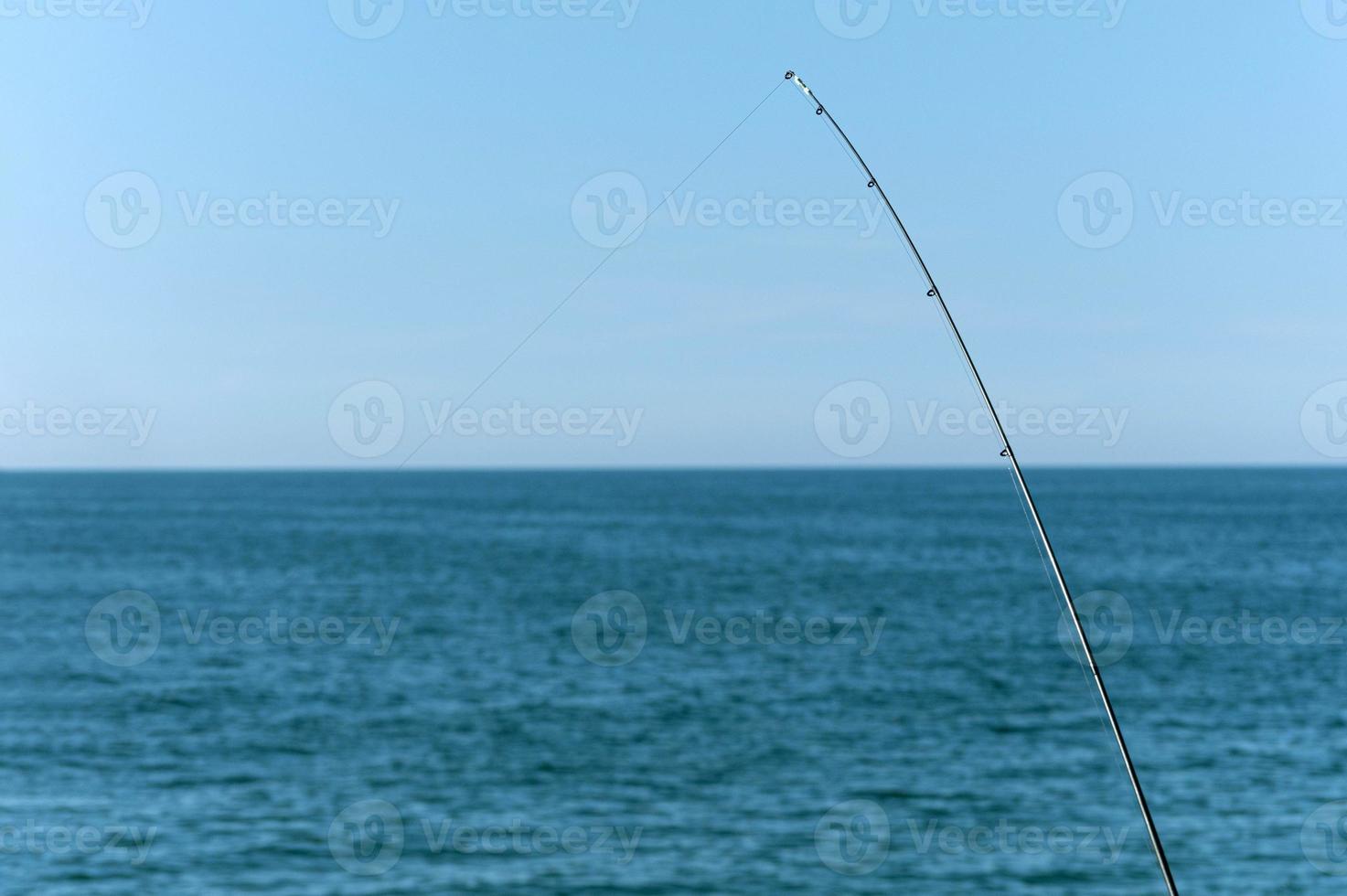 vara de pescar contra o oceano azul ou fundo do mar, copie o espaço. esperando a maior carga. esporte de relaxamento meditativo. foto