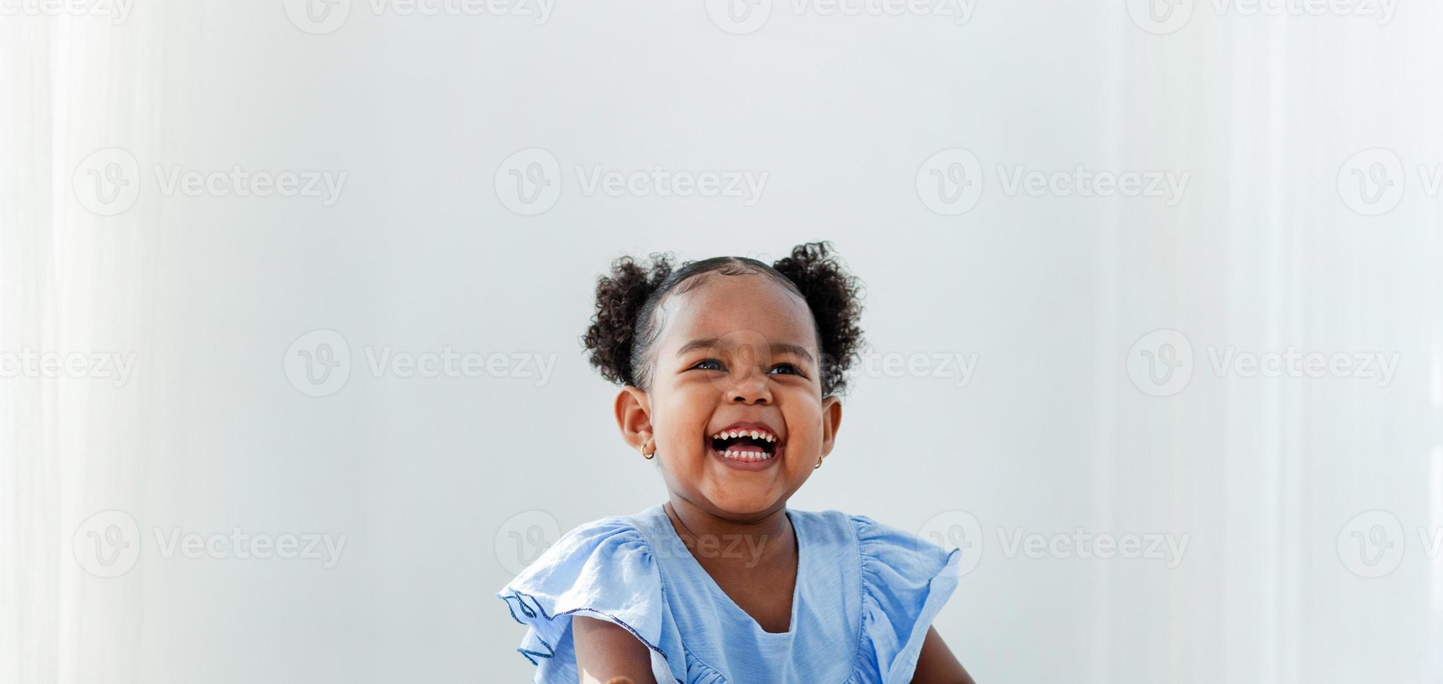menina afro-americana com um lindo vestido azul com fundo branco de sorriso feliz de cabelo encaracolado. crianças felizes em casa foto