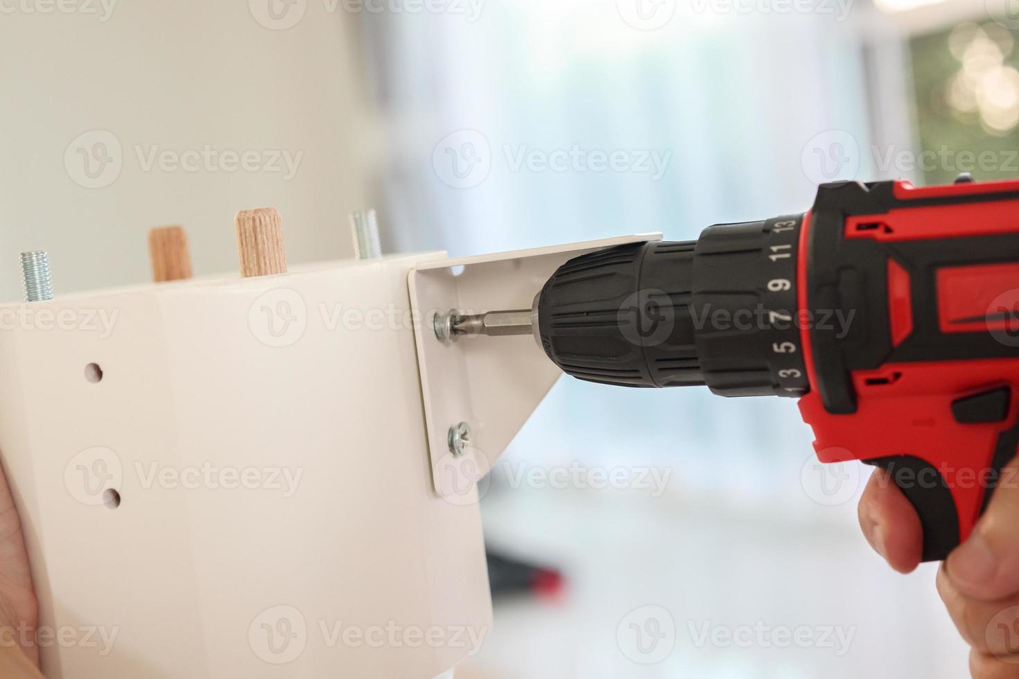 homem montando móveis de mesa branca em casa usando chave de fenda sem fio foto