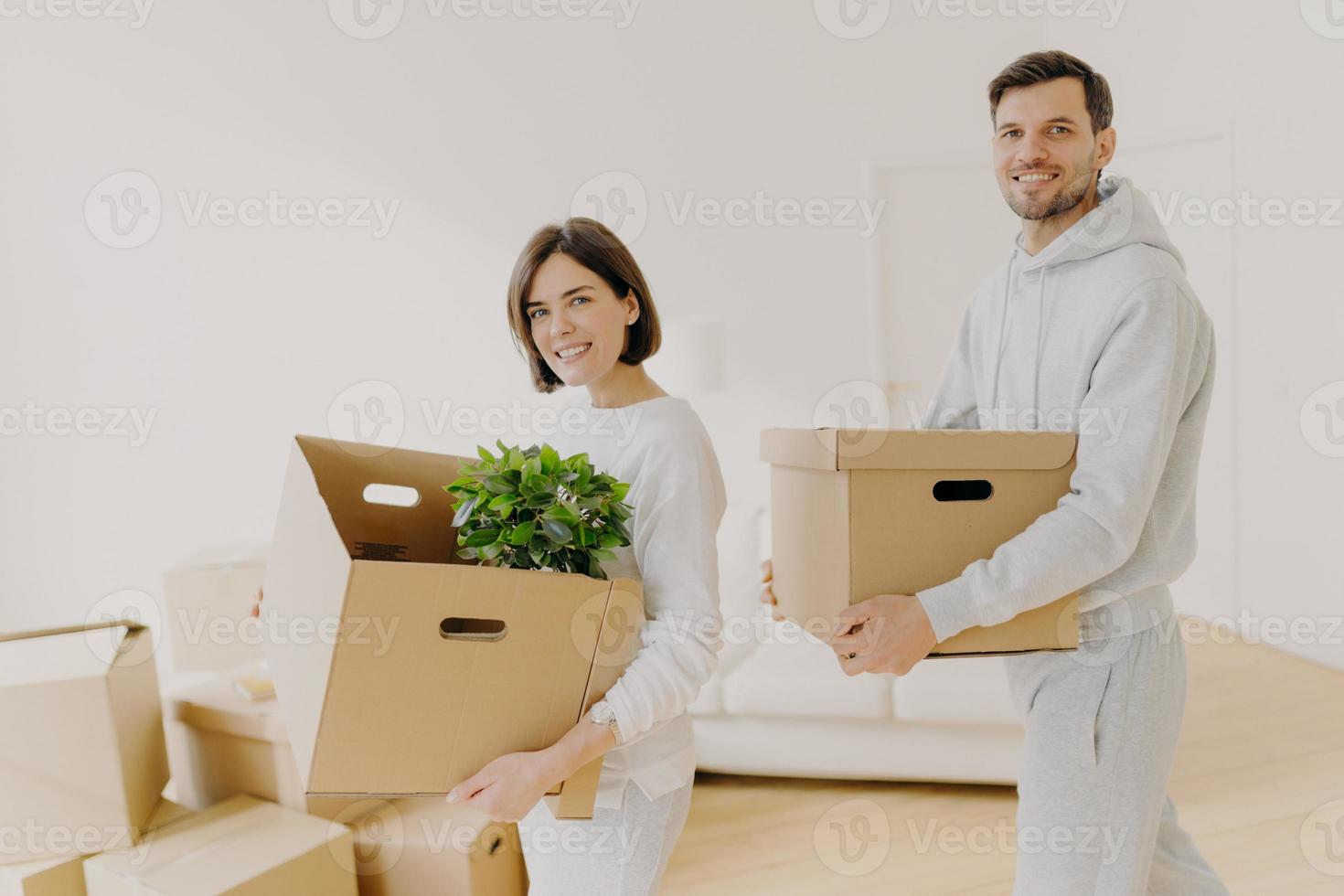 compra de imóveis e conceito de empréstimo hipotecário. feliz mulher e homem carregam caixas de papelão se mudam para uma nova casa, ocupadas em desempacotar. proprietários de propriedades familiares seguram recipientes de papelão com coisas pessoais foto