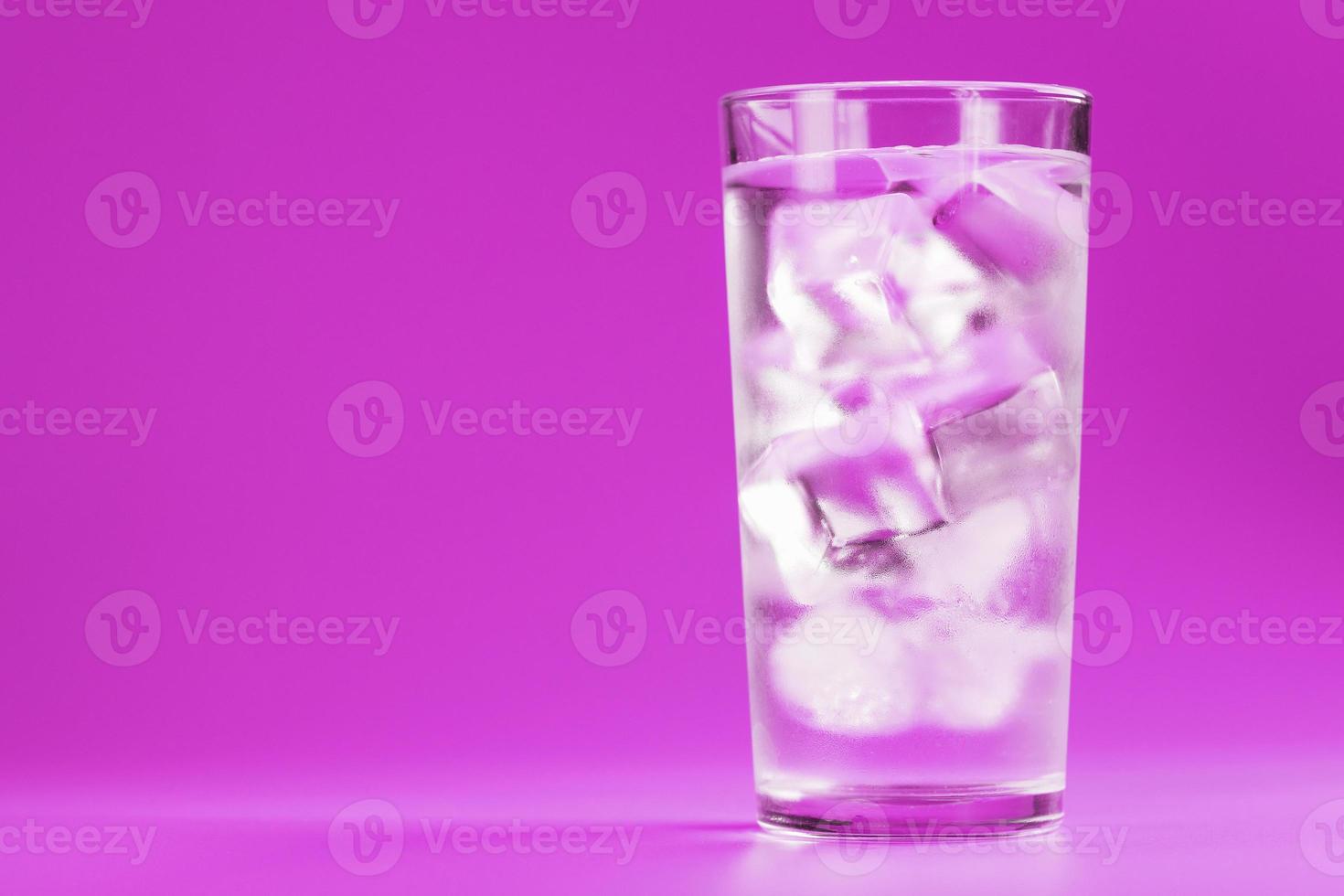 copo com água e cubos de gelo em um fundo rosa foto