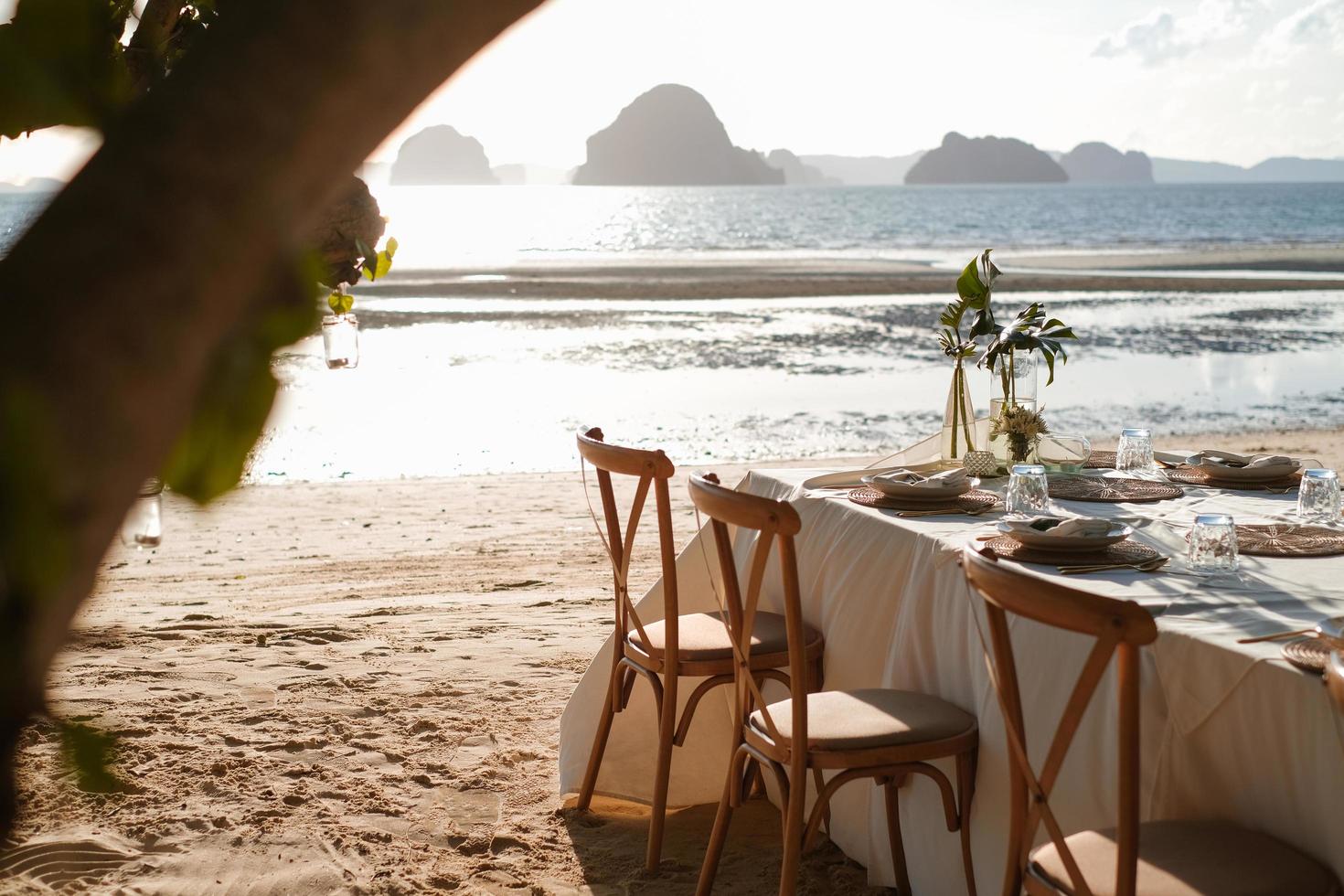 configuração de jantar romântico na praia durante o pôr do sol maravilhoso. preparando-se para uma festa ao ar livre na praia. lugar romântico para lua de mel ou dia do casamento. foco seletivo. foto