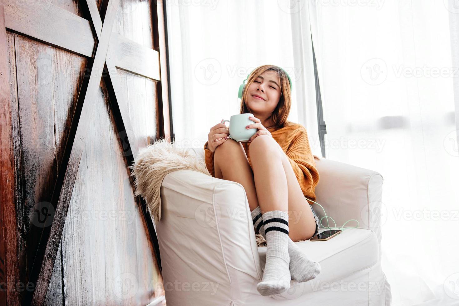 foco suave de jovem feliz relaxando pelo fone de ouvido de música do smartphone no sofá em casa aconchegante, estilo de vida das pessoas modernas foto