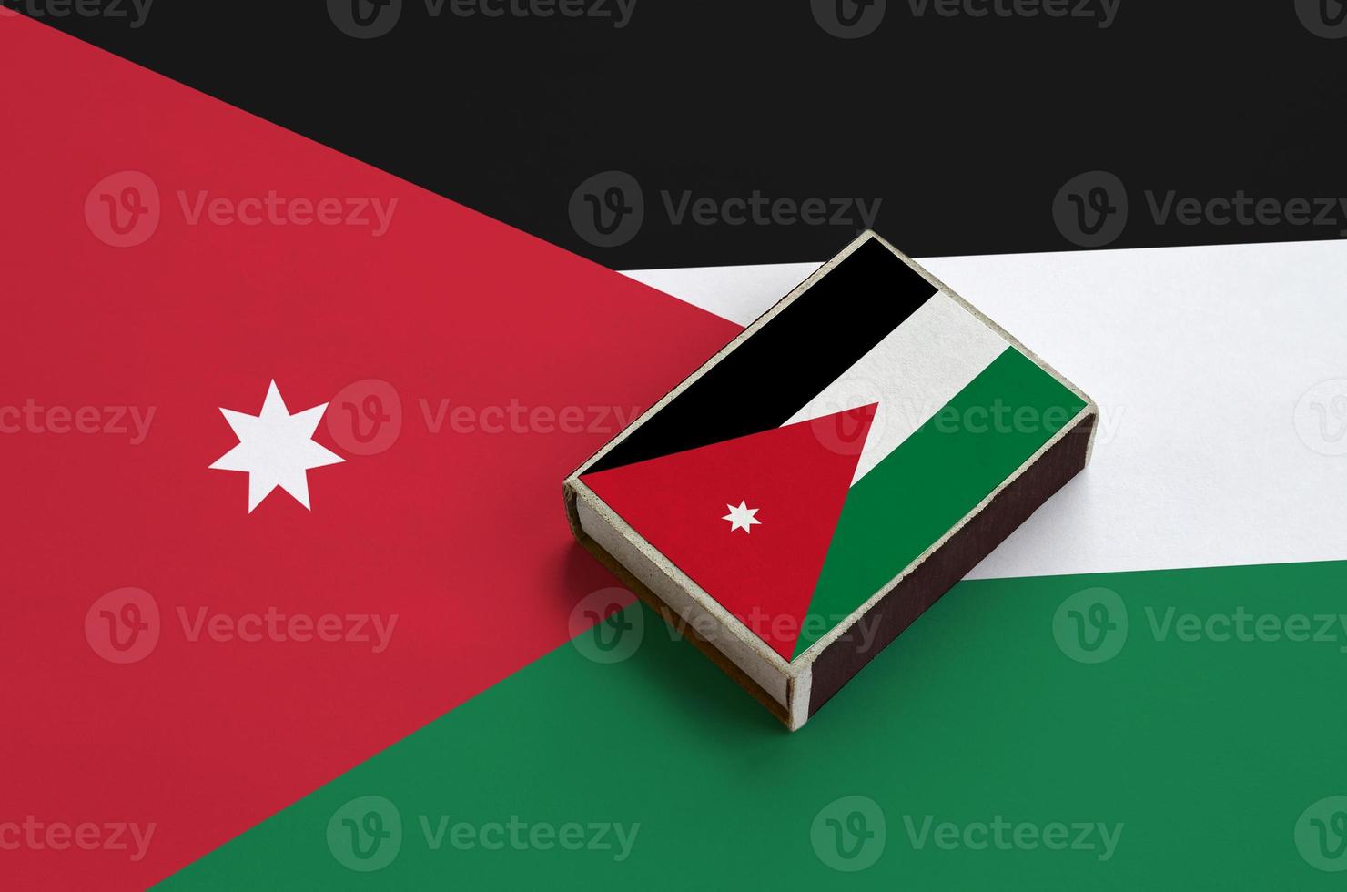 bandeira da jordânia é retratada em uma caixa de fósforos que fica em uma grande bandeira foto