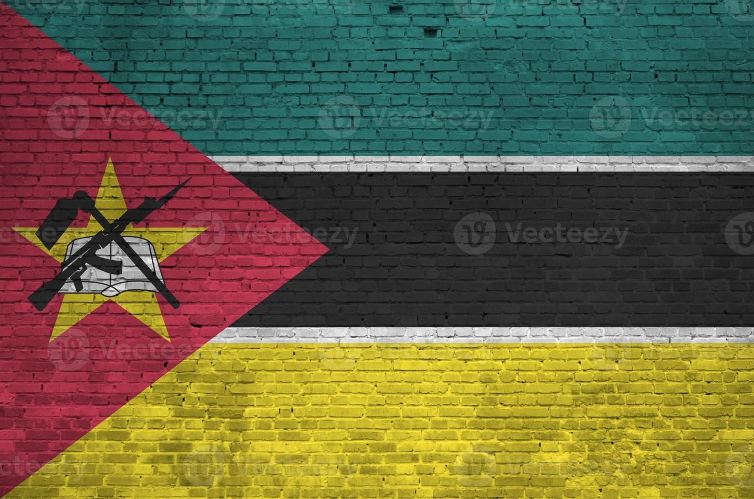 bandeira de moçambique retratada em cores de tinta na parede de tijolos antigos. banner texturizado em fundo de alvenaria de parede de tijolo grande foto