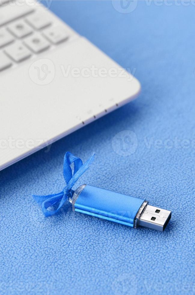 cartão de memória flash usb azul brilhante com um laço azul repousa sobre um cobertor de tecido de lã azul claro macio e peludo ao lado de um laptop branco. design de presente feminino clássico para um cartão de memória foto