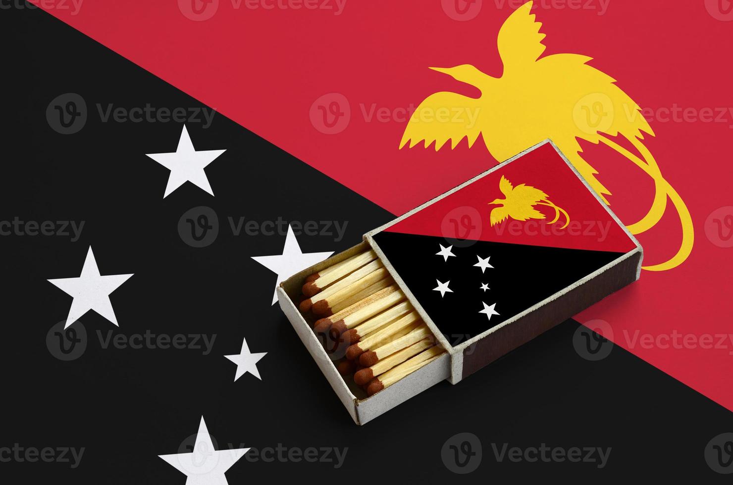 a bandeira de papua nova guiné é mostrada em uma caixa de fósforos aberta, cheia de fósforos e em uma grande bandeira foto