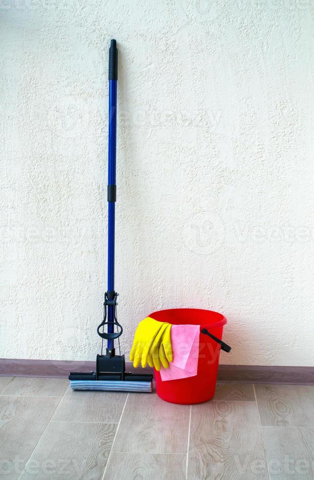 Limpeza de casa. a foto mostra um balde vermelho, luvas de borracha, um pano e um esfregão.