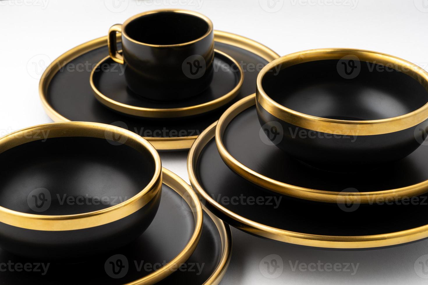 um conjunto de pratos de cerâmica preta e dourada e copo em um fundo branco foto