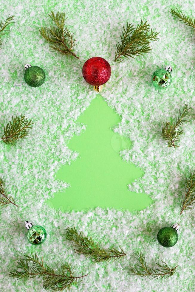 composição de inverno com galhos de abeto decorados com árvore de natal, decorações de natal vermelhas, verdes e prateadas em um fundo verde com neve artificial, configuração plana. cartão de felicitações para o ano novo. foto