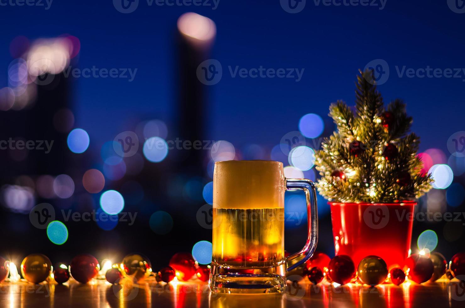 um copo de cerveja coloca na mesa de madeira que tem enfeites de árvore de natal e bugigangas com luz de fundo colorido bokeh da cidade. foto