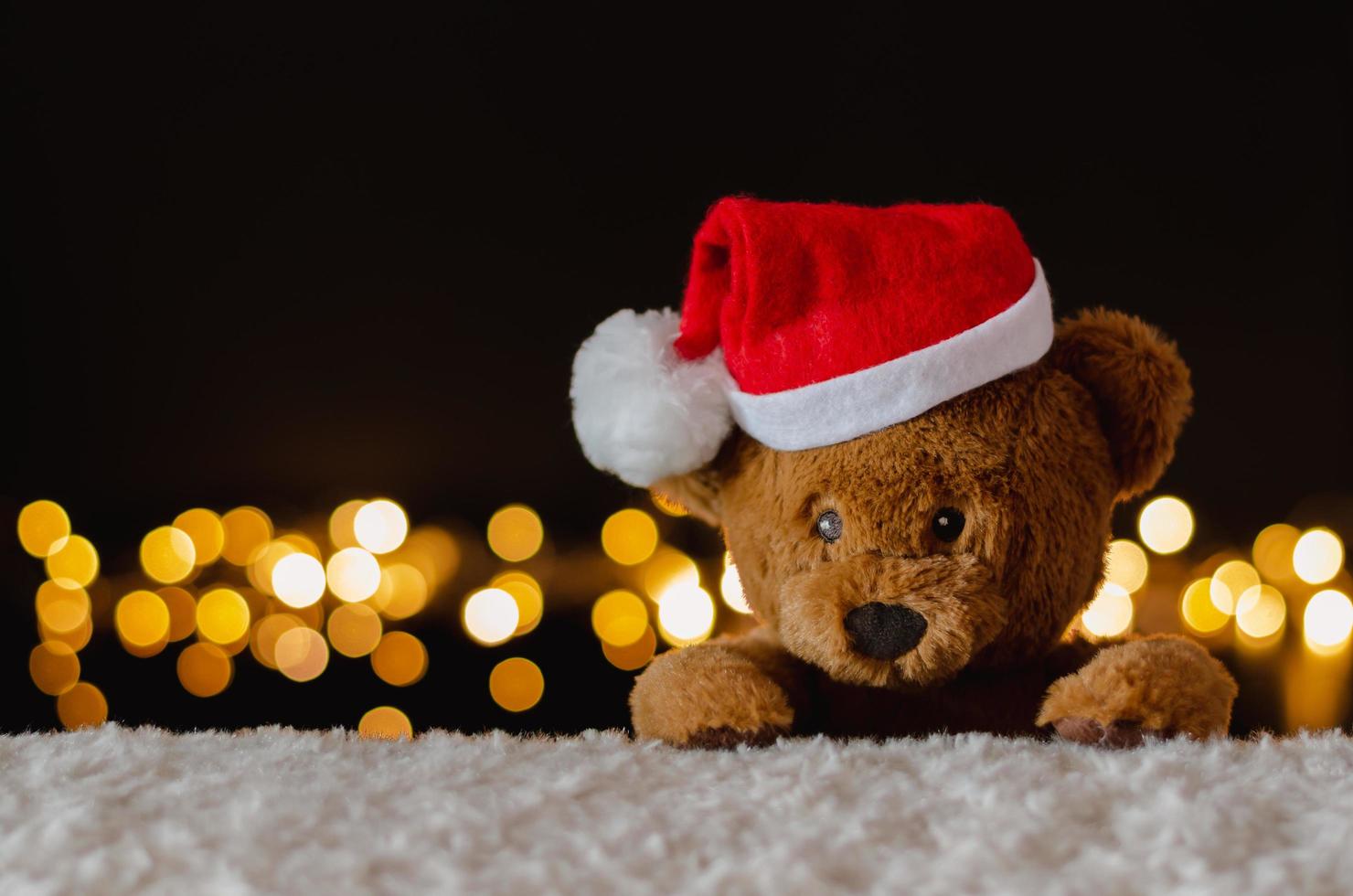 urso de pelúcia marrom com chapéu de papai noel com fundo de luzes de natal. foto