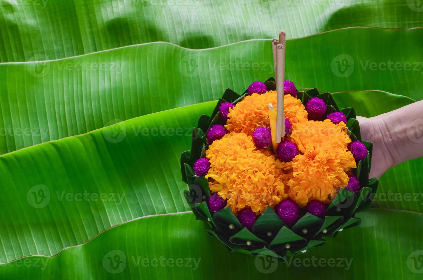 mão segurando folha de bananeira krathong que tem 3 incensos e vela decora com flores para a lua cheia da tailândia ou festival loy krathong. foto