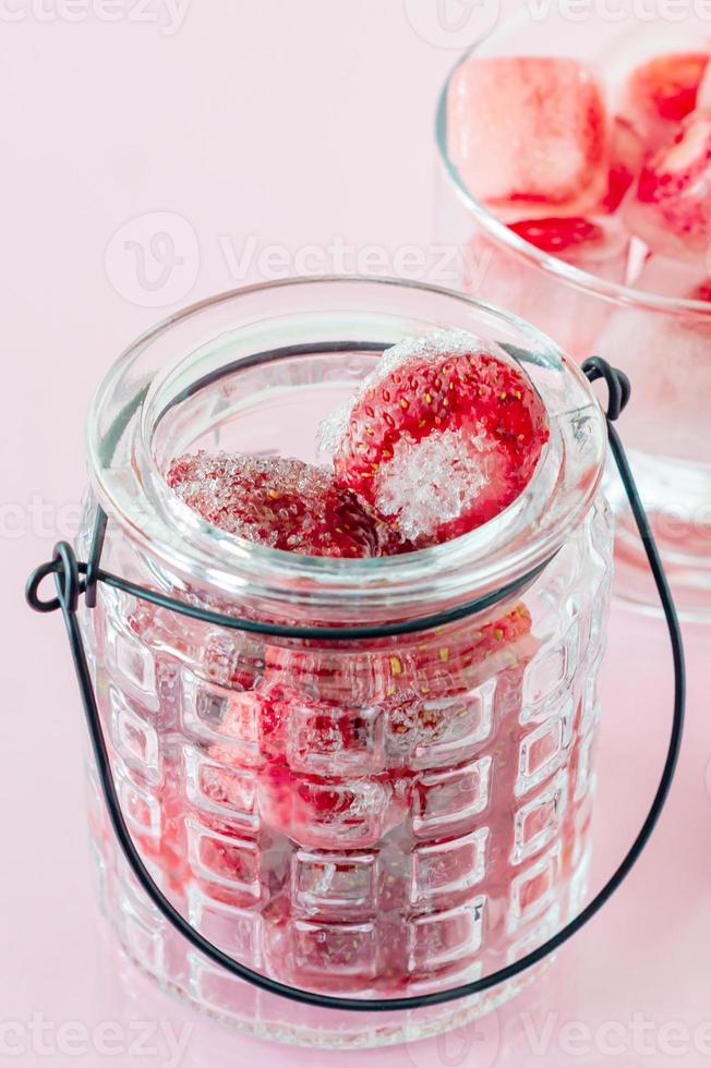 morango congelado com cristais de gelo no fundo rosa foto