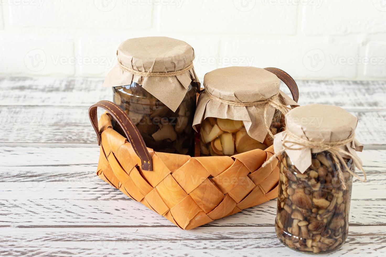 frascos de vidro com cogumelos enlatados em uma cesta. comida fermentada em um fundo branco com espaço de cópia foto