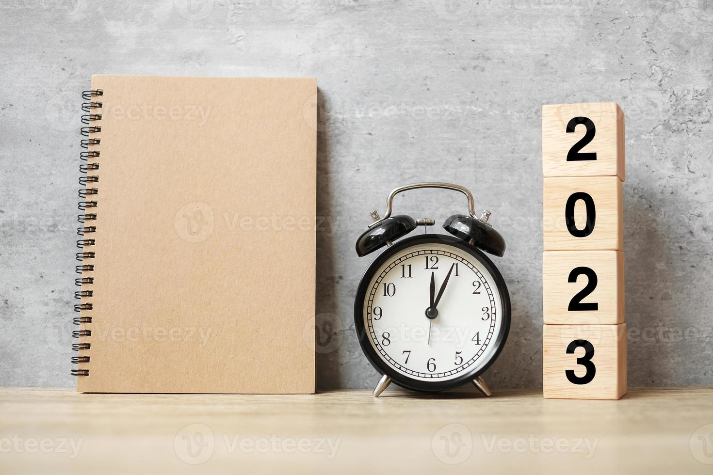 2023 feliz ano novo com caderno em branco, despertador retrô preto e número de madeira. contagem regressiva, resolução, objetivos, plano, ação e conceito de missão foto