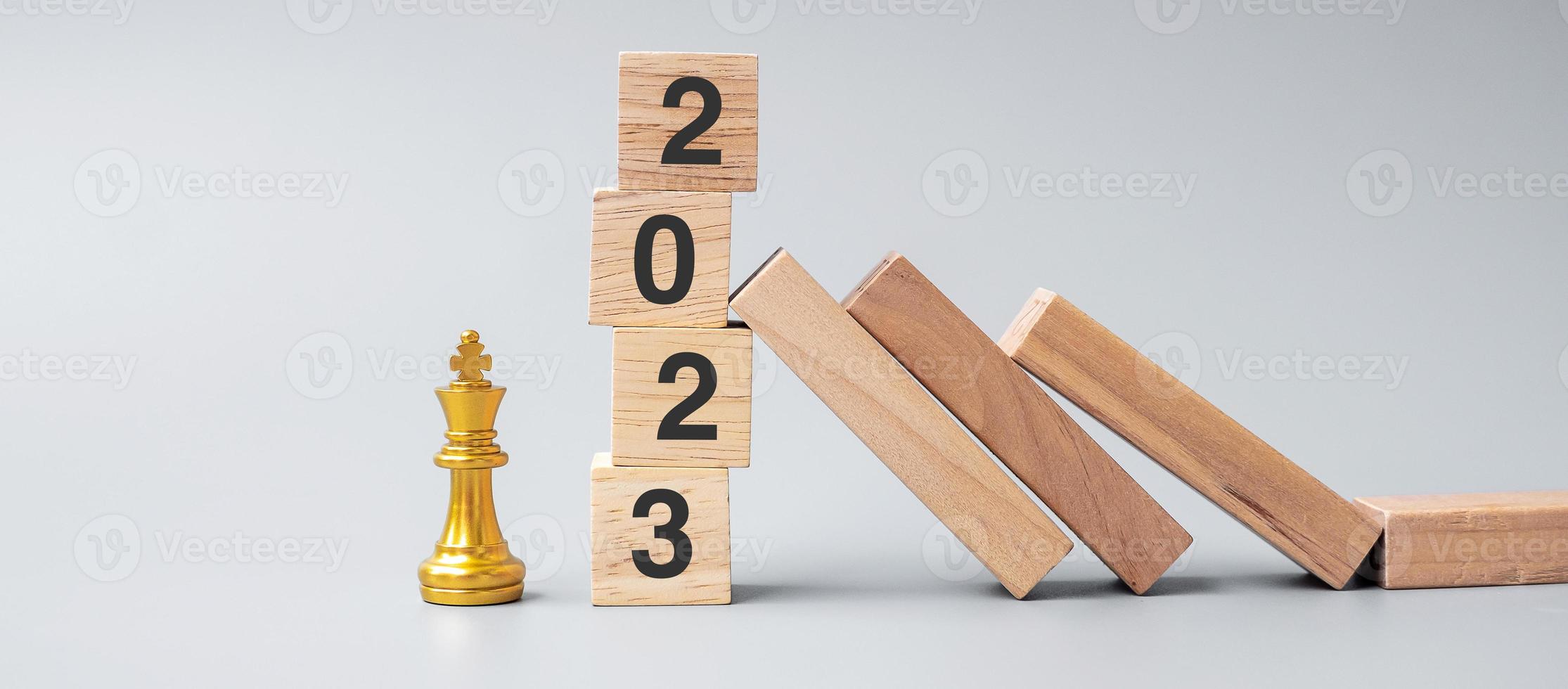 dominós de madeira caindo contra blocos de parada de 2023 com figura dourada do rei do xadrez. negócios, gerenciamento de riscos, solução, conceito econômico, seguro e ano novo foto