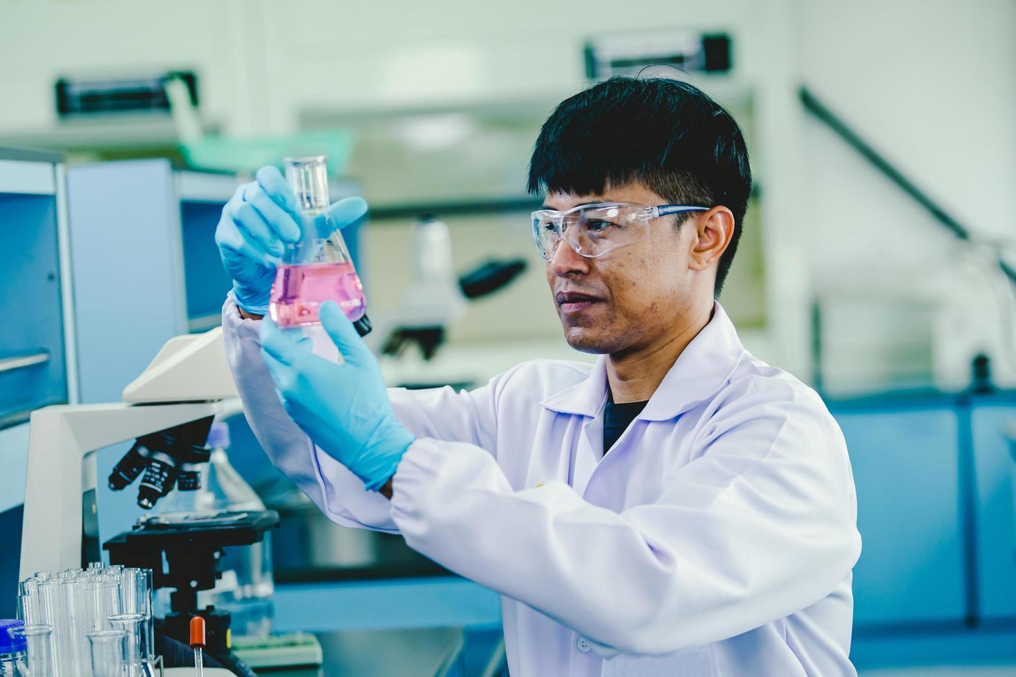 químico masculino asiático usando óculos e laboratório branco trabalhando em laboratório foto