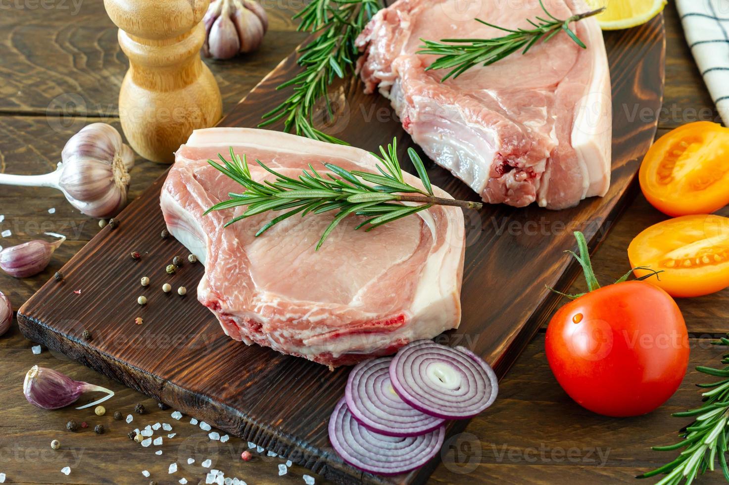pedaços de bife de porco cru com especiarias e ervas alecrim, sal e pimenta na placa de madeira sobre fundo de madeira em estilo rústico foto