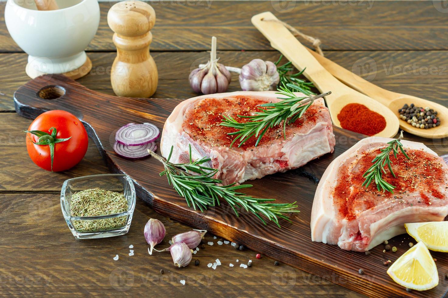 pedaços de bife de porco cru com especiarias e ervas alecrim, sal e pimenta na placa de madeira sobre fundo de madeira em estilo rústico foto