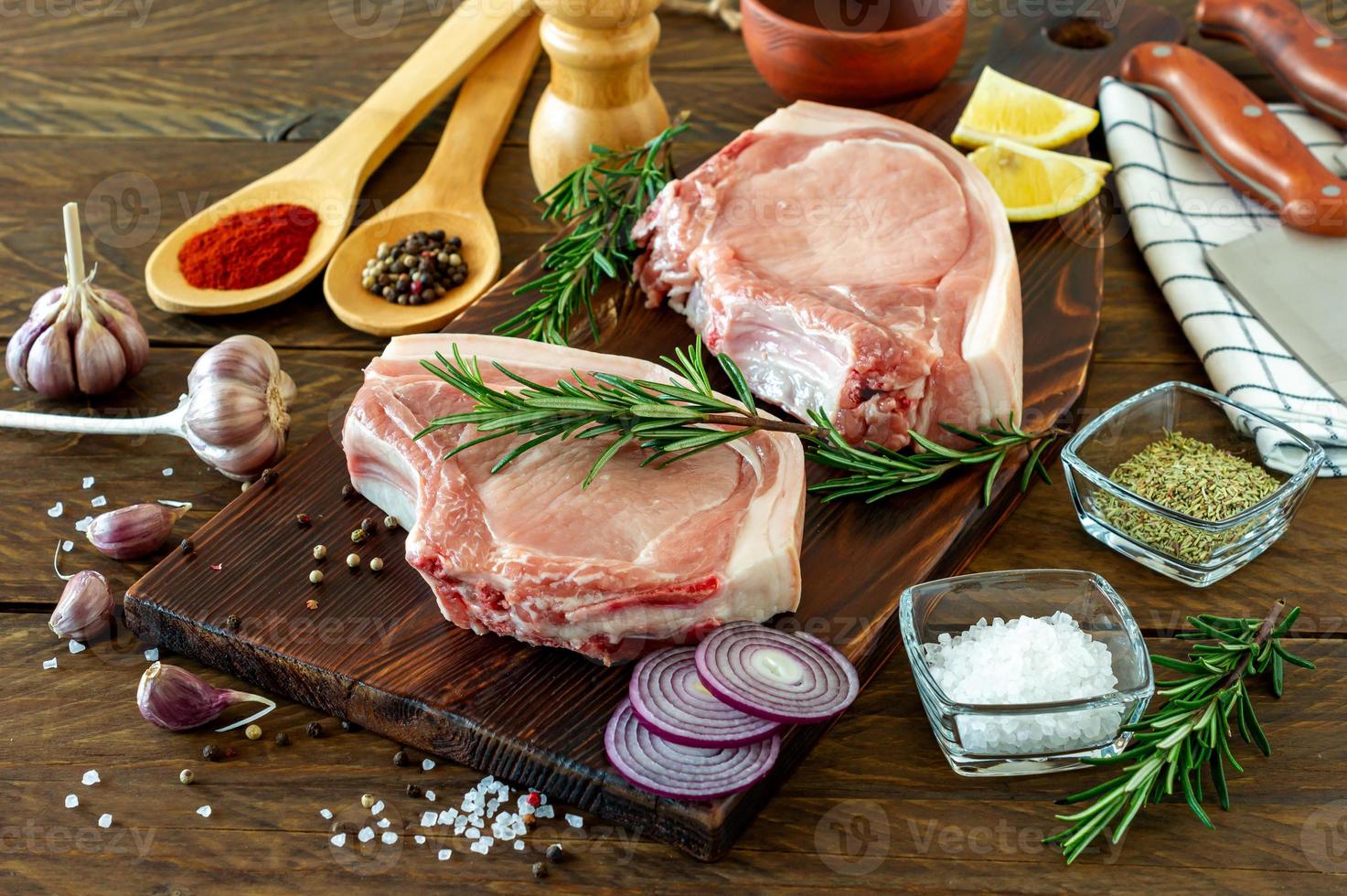 pedaços de bife de porco cru com especiarias e ervas alecrim, sal e pimenta em fundo de madeira em estilo rústico foto