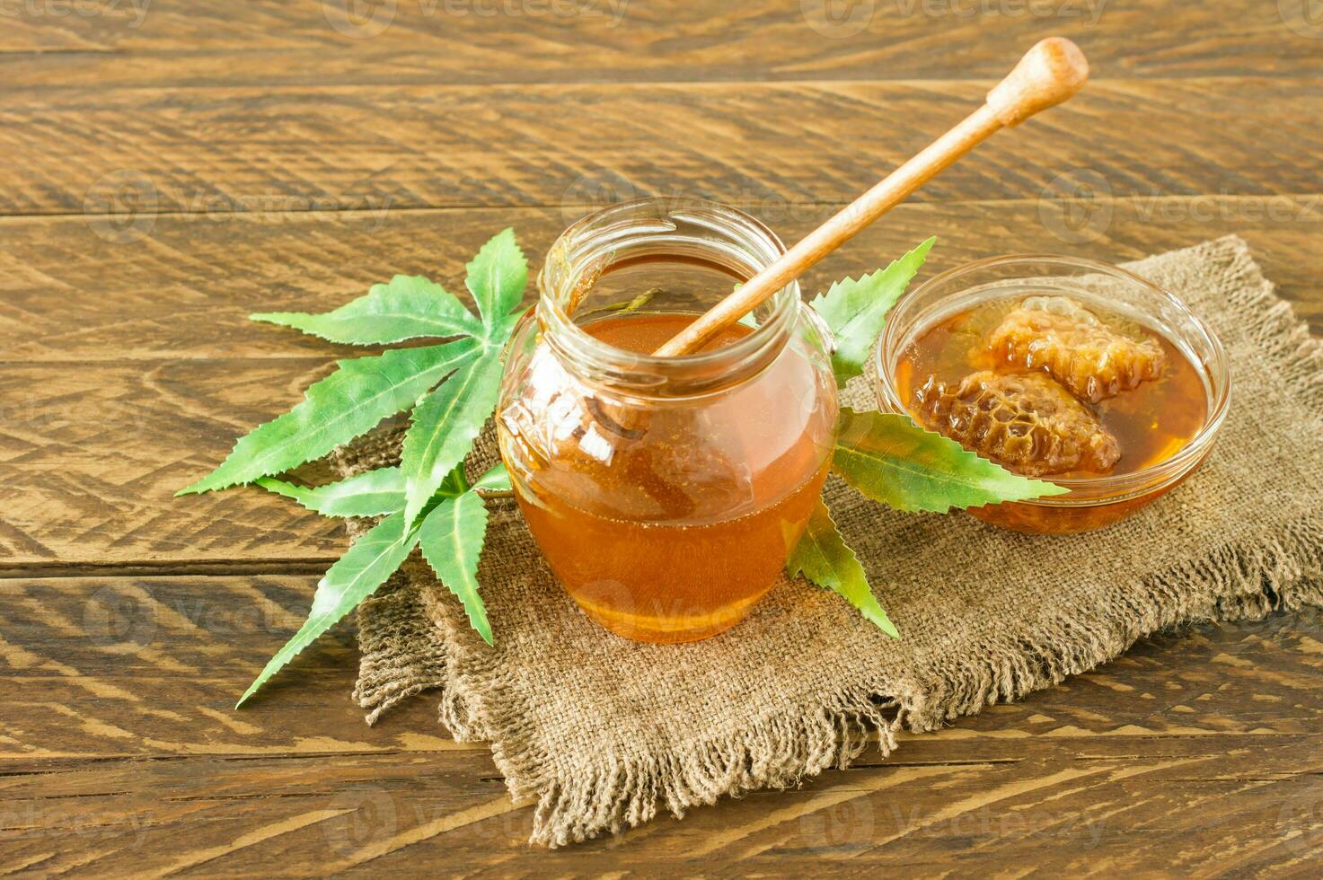 folhas de cannabis, maconha e mel puro orgânico fresco em frasco de vidro no fundo da mesa de madeira. conceito cbd de mel. foto