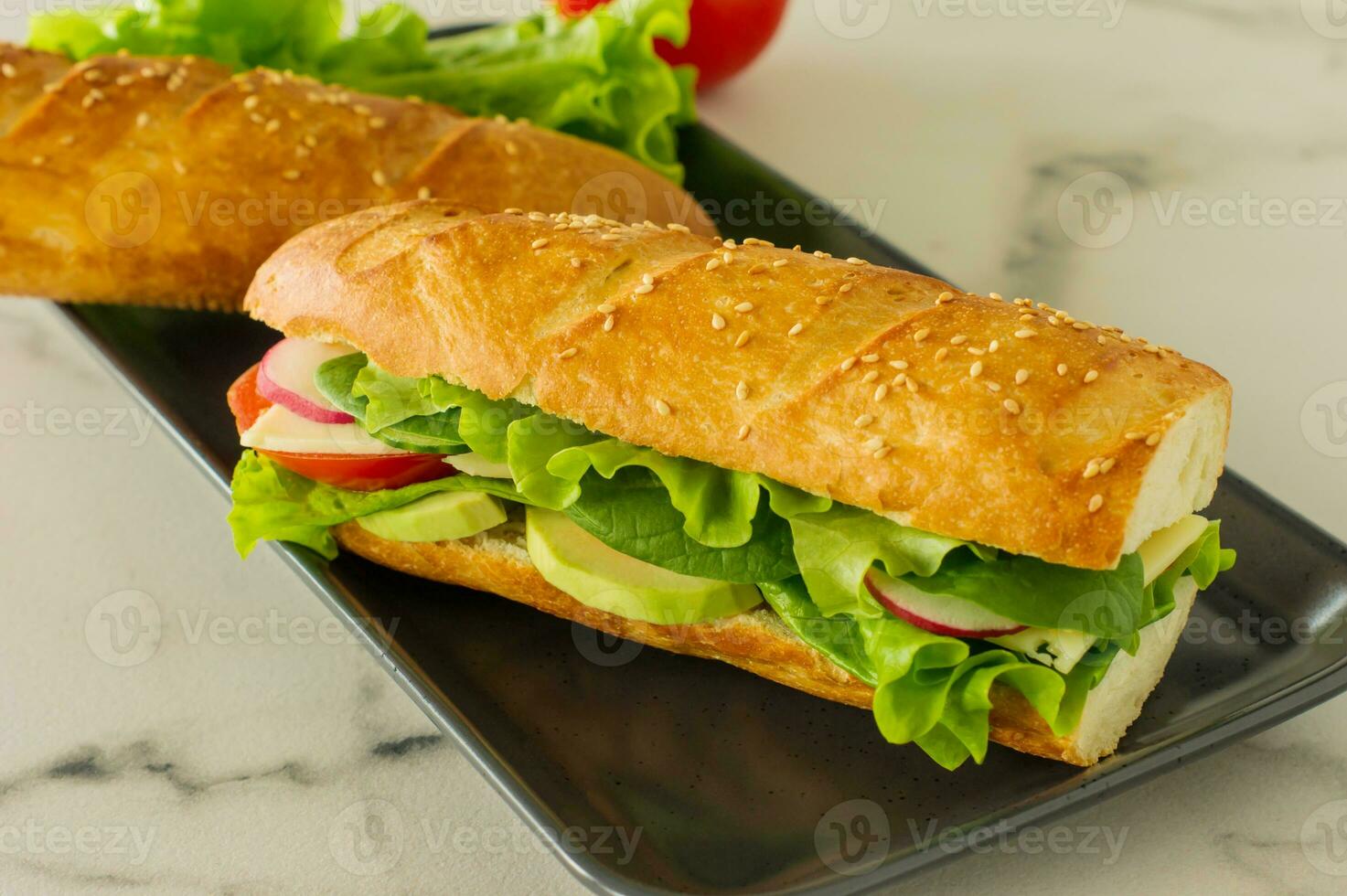 Sanduíche vegano de baguete longa integral com alface, abacate, tomate e queijo. lanche saudável e comida para viagem foto