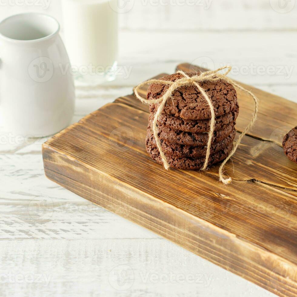 biscoitos de chocolate no café da manhã com um copo de leite em uma mesa de madeira branca. foto