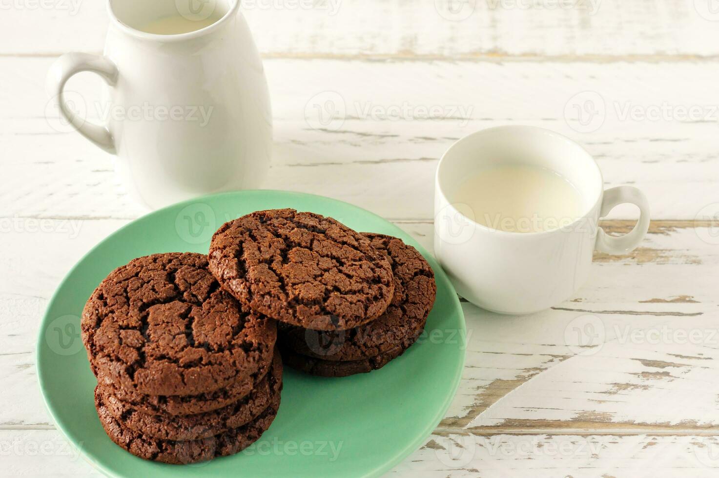 biscoitos de chocolate no café da manhã com um copo de leite em uma mesa de madeira branca. foto