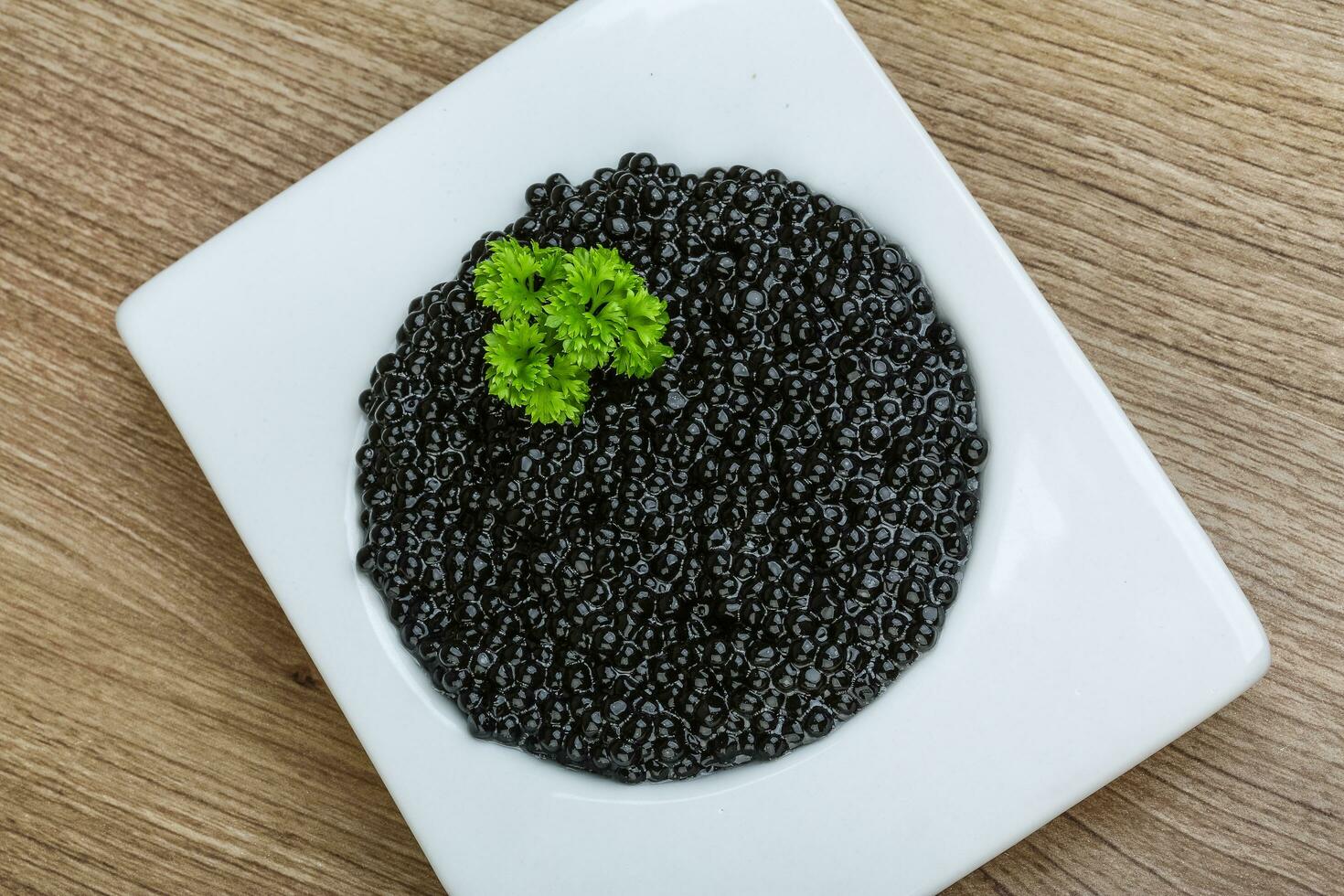 caviar preto em uma tigela sobre fundo de madeira foto