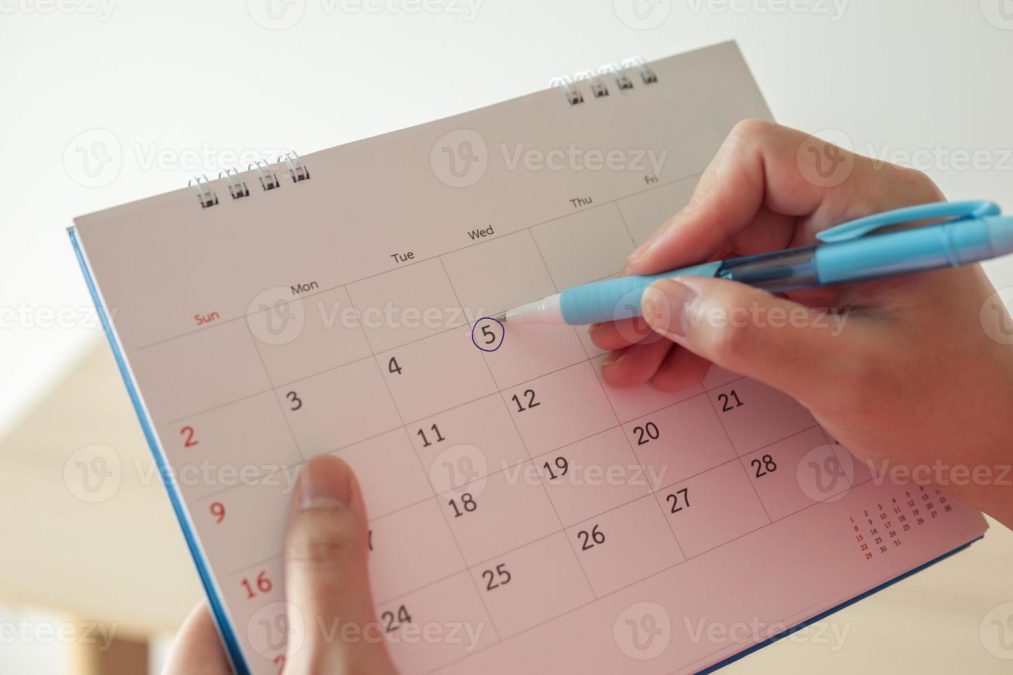 mão com marca de caneta no dia 5 na data do calendário com círculo azul foto