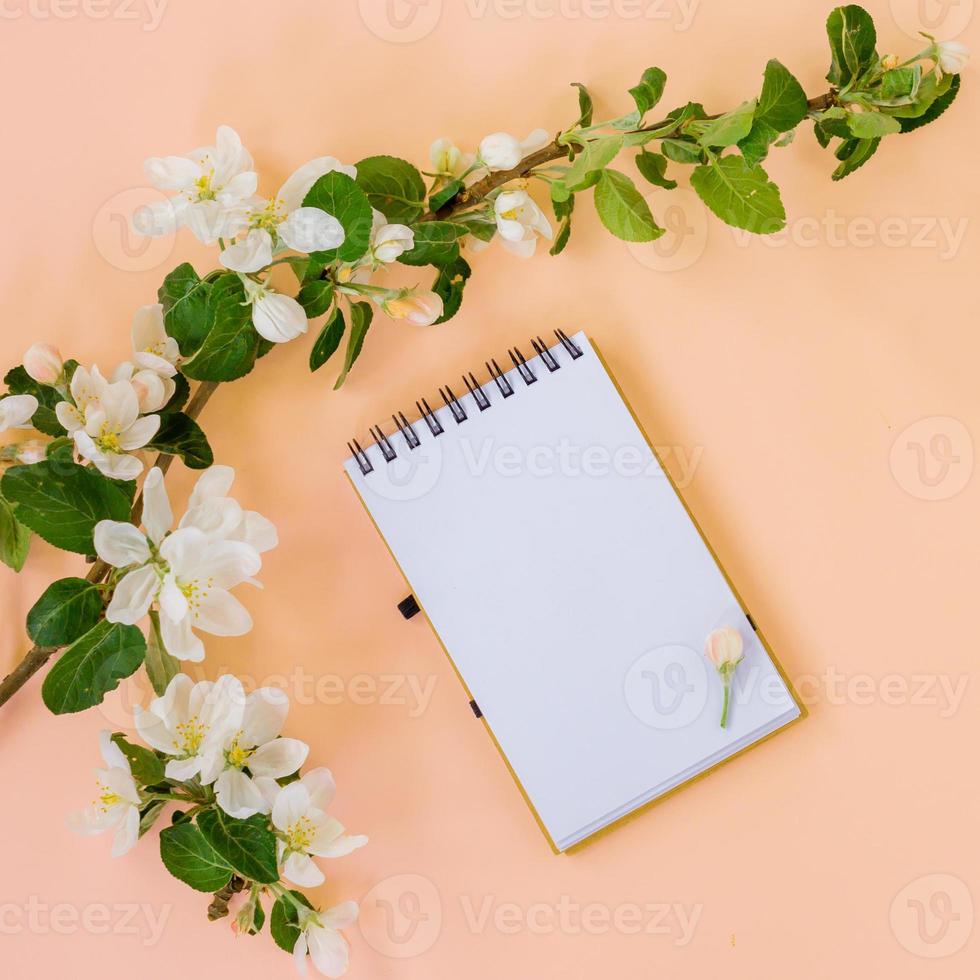 configuração plana criativa do quadro de bloco de notas espiral em branco simulado e pétalas de flores de macieira em fundo rosa pastel com espaço de cópia em estilo minimalista, modelo para letras, texto ou seu design foto