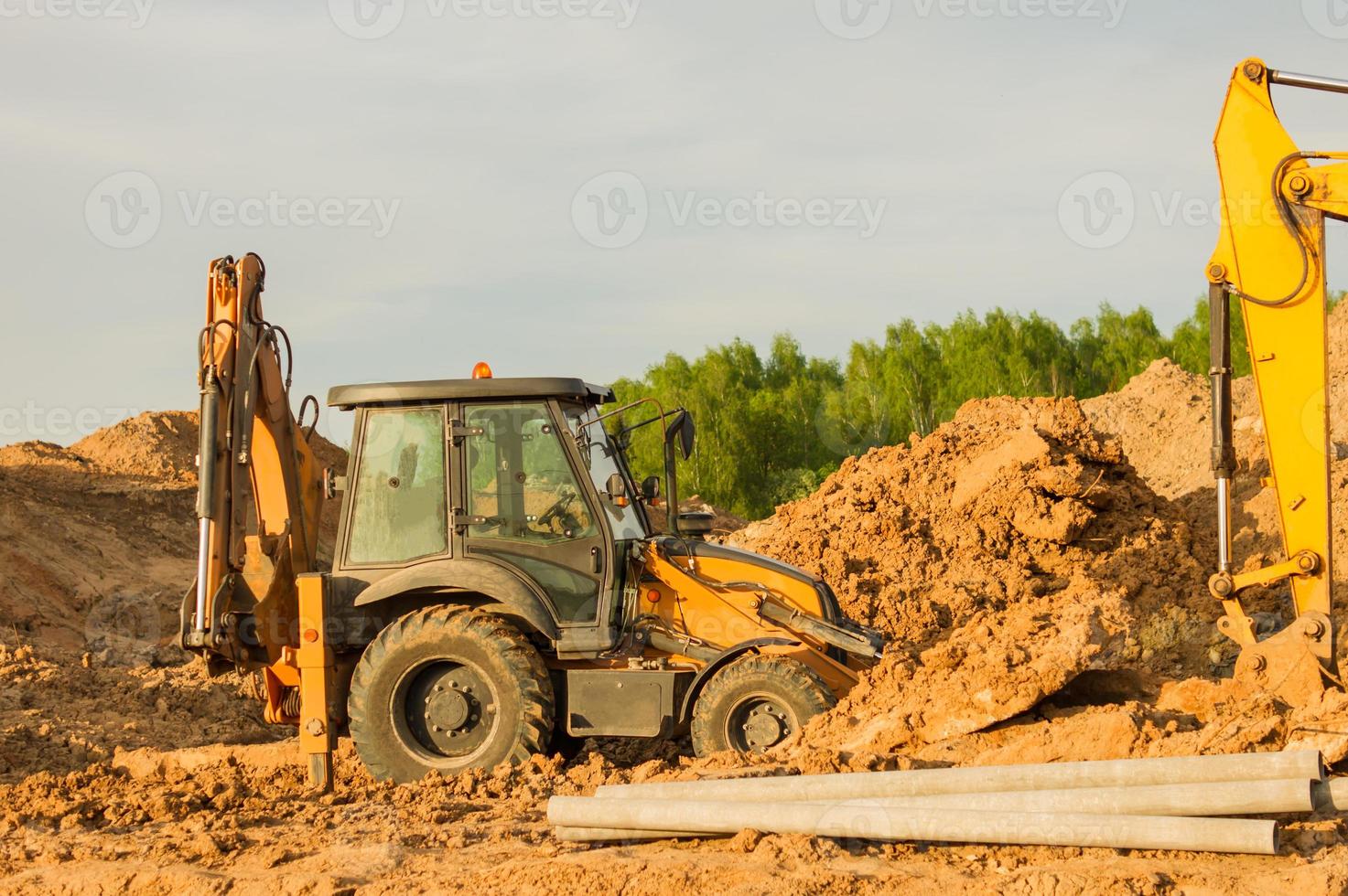 escavadeira amarela durante a terraplanagem no canteiro de obras. retroescavadeira cavando o terreno para a fundação e para a colocação de tubos de esgoto aquecimento urbano. equipamento pesado de terraplanagem foto