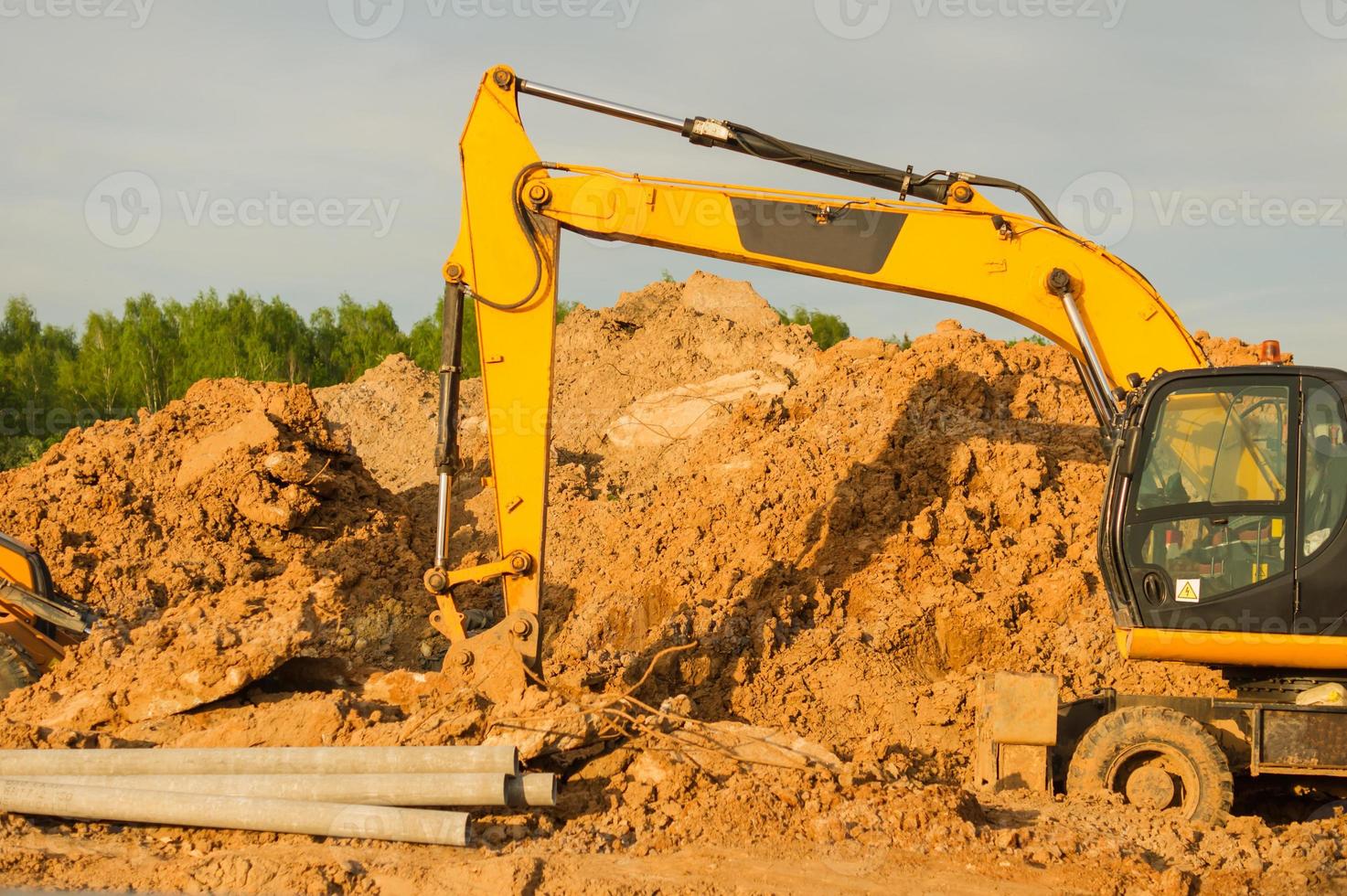 escavadeira amarela durante a terraplanagem no canteiro de obras. retroescavadeira cavando o terreno para a fundação e para a colocação de tubos de esgoto aquecimento urbano. equipamento pesado de terraplanagem foto