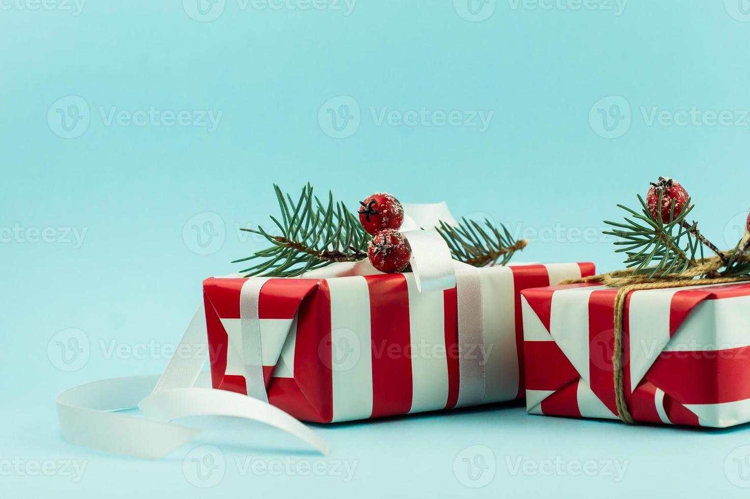 dois presentes festivos em embalagens vermelhas e brancas com elementos decorativos de ramos de abeto e bagas com uma fita branca. fundo azul. foto