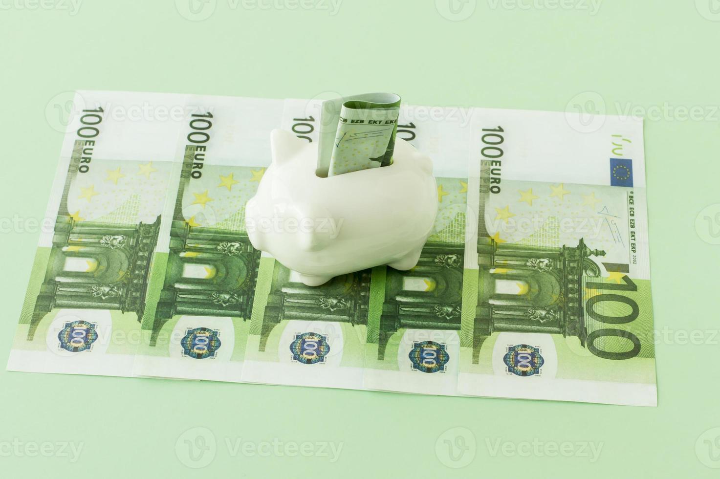 notas de moeda europeia em 100 euros em um fundo verde com um cofrinho de porcelana branca nas notas. foto