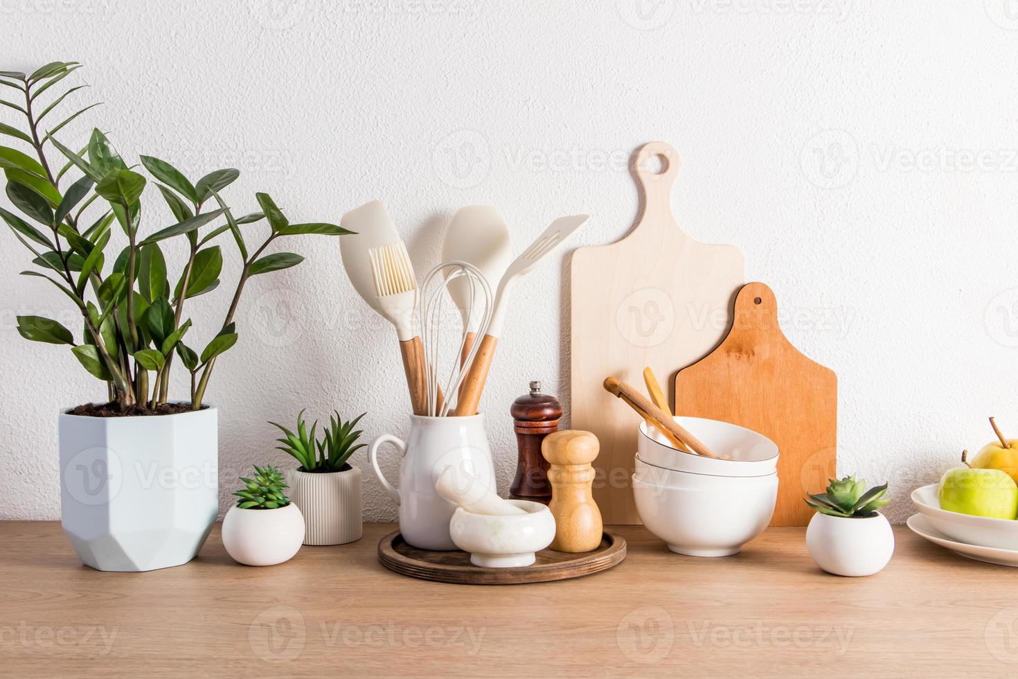 uma variedade de utensílios de cozinha, uma flor em vaso e frutas em um prato em uma bancada de madeira contra uma parede texturizada branca. vista frontal. foto