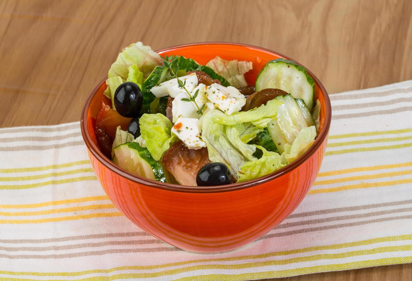 salada grega em uma tigela sobre fundo de madeira foto