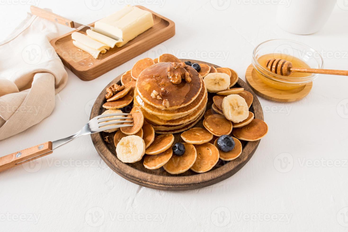 panquecas caseiras com mel, nozes e frutas em uma placa de madeira em uma mesa branca. o conceito de um café da manhã saudável, lanche. foto