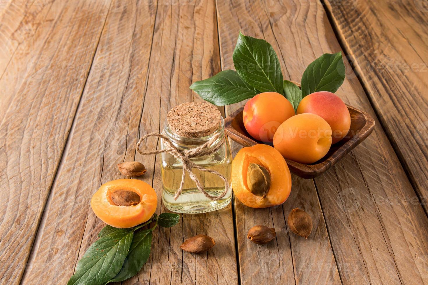 garrafa de vidro de óleo de semente de damasco em uma mesa de aldeia de madeira contra um pano de fundo de frutas maduras. o conceito de autocuidado orgânico natural. foto