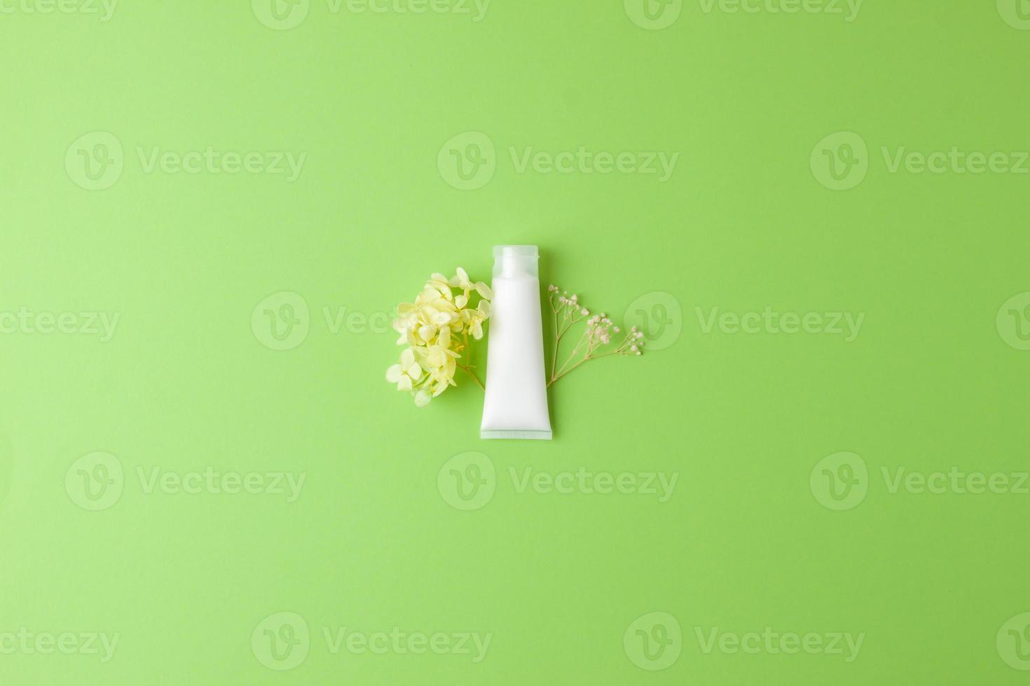 tubo branco de creme cosmético com flores sobre fundo verde. postura plana, copie o espaço foto