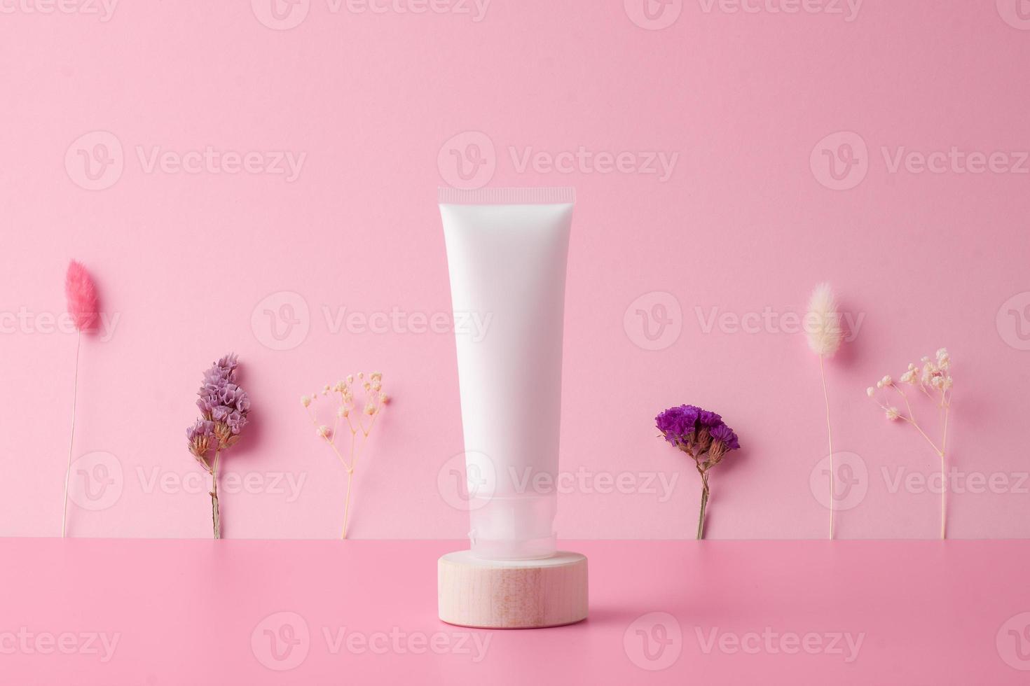 tubo branco de creme cosmético com flores no pódio de madeira no fundo rosa. fechar-se. foto