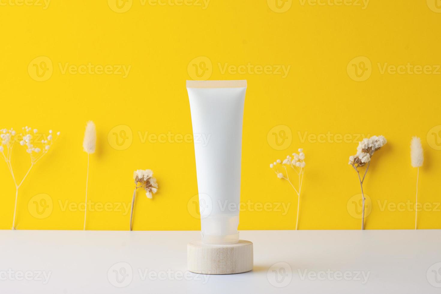 tubo branco de creme cosmético com flores no pódio de madeira sobre fundo amarelo. fechar-se. foto